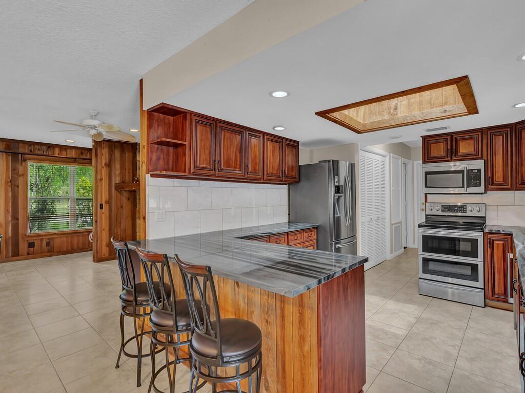 A kitchen features wood cabinets, a stone-patterned breakfast bar, and a recessed ceiling light — 725 4th Avenue SW, Vero Beach FL 32962, VERO BEACH, FL