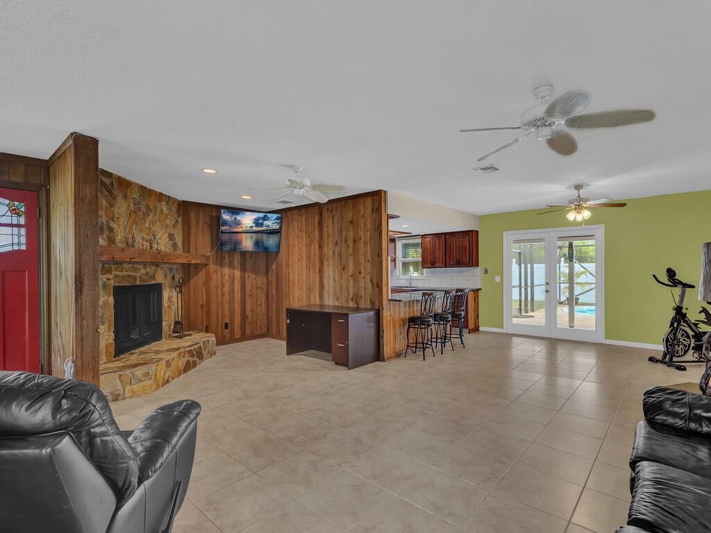 A living room with a stone fireplace, wood paneling, tile floors, and an adjacent kitchen — 725 4th Avenue SW, Vero Beach FL 32962, VERO BEACH, FL