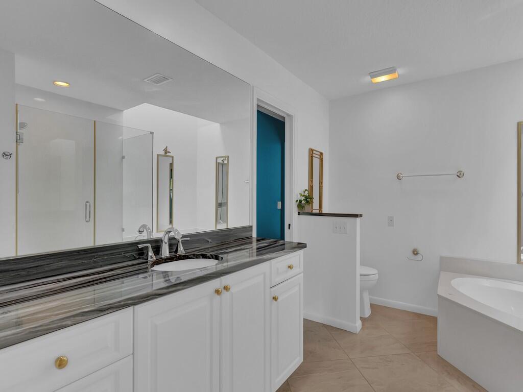 A bathroom features a white vanity with a dark stone countertop, a mirror, and tub — 725 4th Avenue SW, Vero Beach FL 32962, VERO BEACH, FL