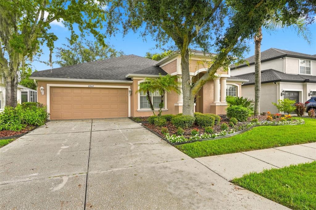 A single-story house with a tan stucco exterior, a two-car garage, and a columned entryway — 27417 SILVER THATCH DRIVE, WESLEY CHAPEL, FL