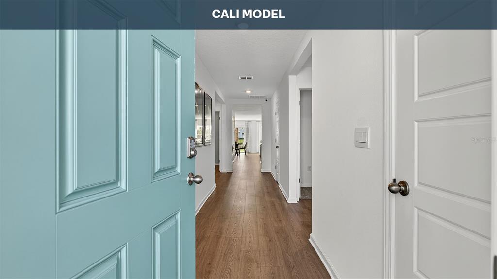 A view from an open teal front door looking down a hallway with wood flooring — 73 SAWDUST LANE, PALM COAST, FL