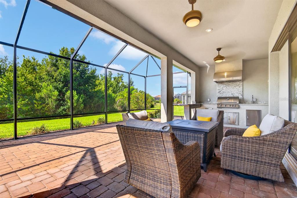 A covered patio features a brick floor, outdoor kitchen, and wicker furniture inside a screened enclosure — 10924 WICKER PARK PLACE, PALMETTO, FL