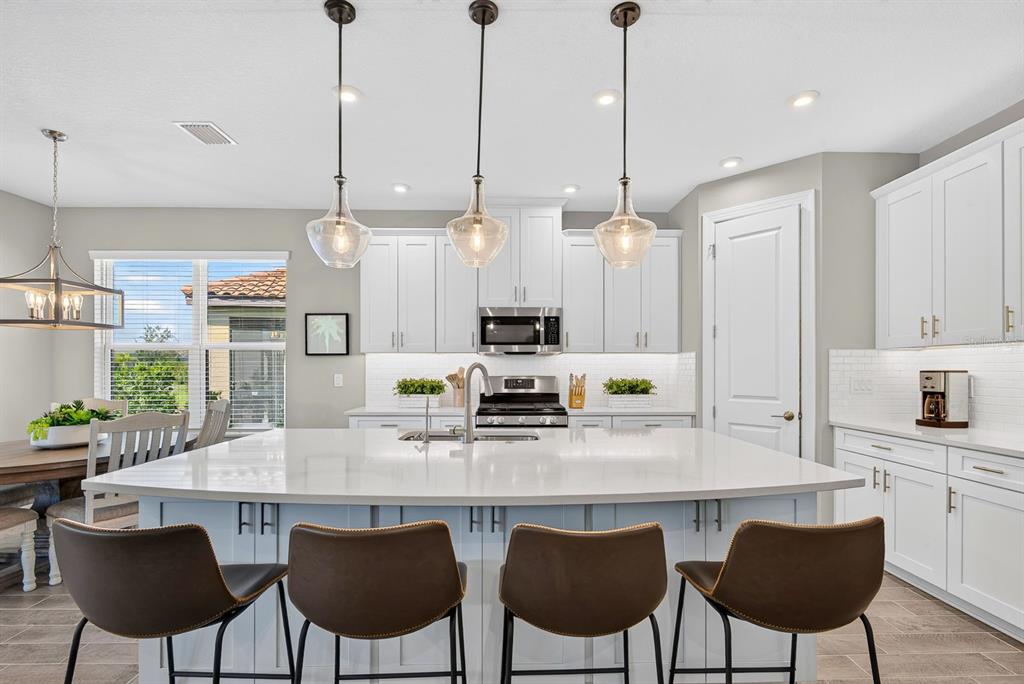 A kitchen features a large white island with bar seating, pendant lights, and white cabinetry — 10924 WICKER PARK PLACE, PALMETTO, FL