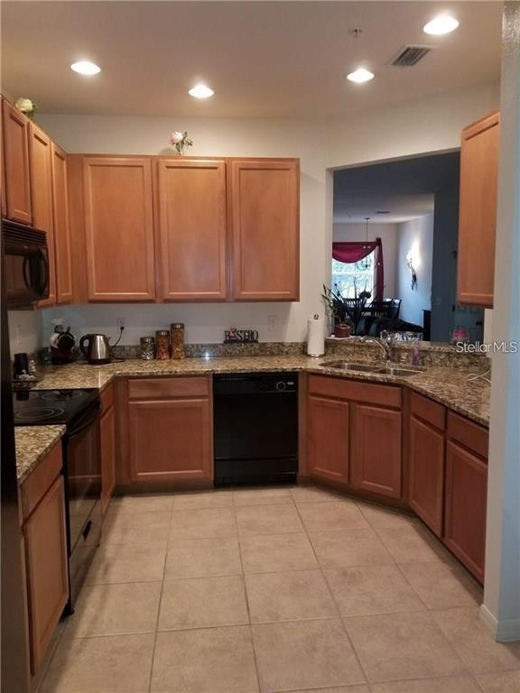 A kitchen features light wood cabinets, granite countertops, tile flooring, and a black dishwasher — 3661 PARKRIDGE CIRCLE UNIT 9-104, SARASOTA, FL