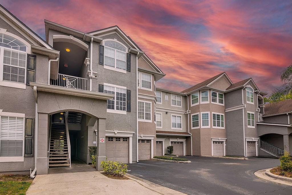 A multi-story apartment building with gray stucco siding, attached garages, and an exterior staircase — 3307 S KIRKMAN ROAD UNIT 126, ORLANDO, FL