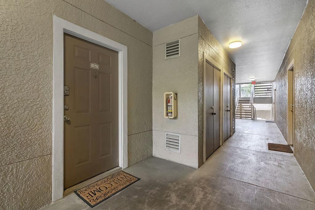 An exterior apartment hallway features a brown door labeled 126, a fire extinguisher, and stairs — 3307 S KIRKMAN ROAD UNIT 126, ORLANDO, FL