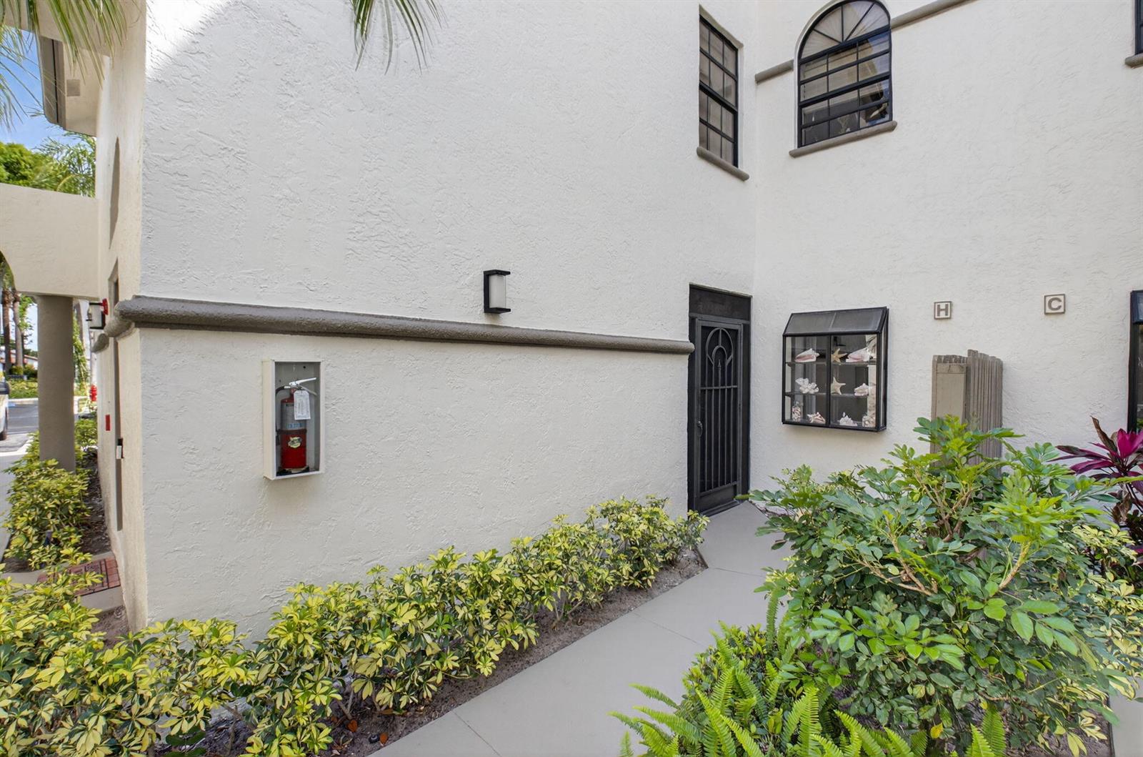 A white stucco building exterior features a walkway, a fire extinguisher, and a black door — 5226 Europa Drive # H, Boynton Beach FL 33437, BOYNTON BEACH, FL