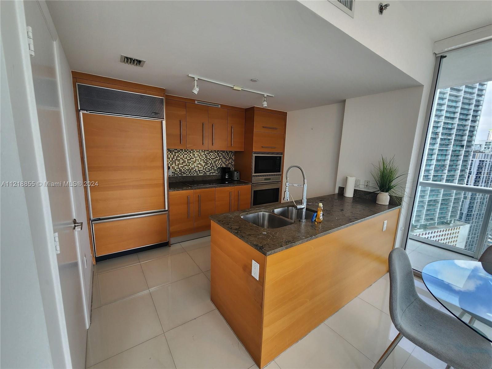 A modern kitchen features wood cabinetry, a stone island with a sink, and floor-to-ceiling windows — 485 Brickell Ave # 2504, Miami FL 33131, MIAMI, FL