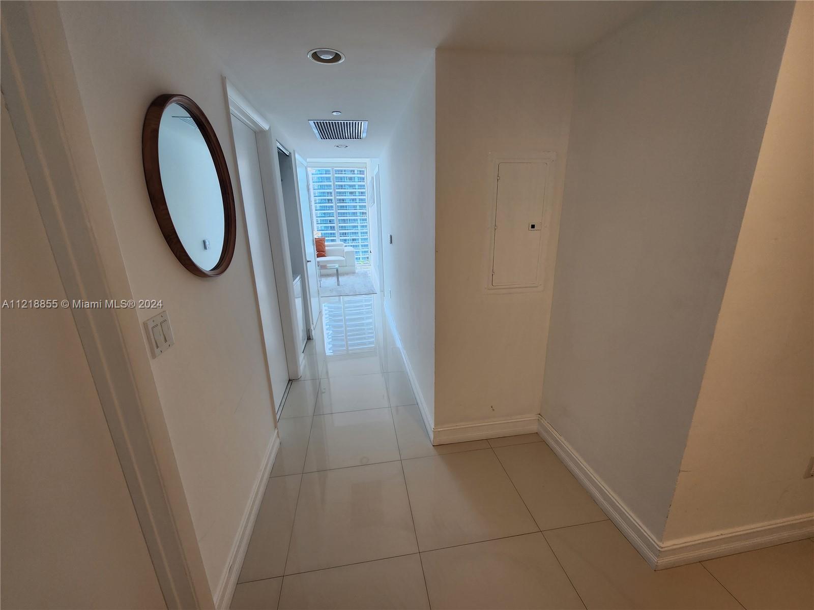A hallway with white walls and light-colored tile flooring leads toward a windowed room — 485 Brickell Ave # 2504, Miami FL 33131, MIAMI, FL