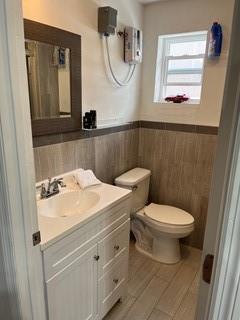 A small bathroom features a white vanity, a toilet, a mirror, and wood-look tile flooring — 2810 NE 7th Avenue, Pompano Beach FL 33064, POMPANO BEACH, FL