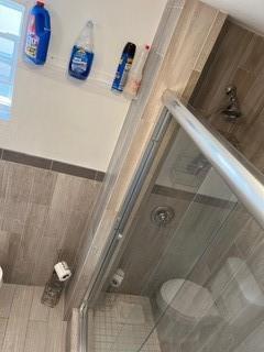 A bathroom features a glass-enclosed shower, wood-look tile walls, and cleaning supplies on a shelf — 2810 NE 7th Avenue, Pompano Beach FL 33064, POMPANO BEACH, FL