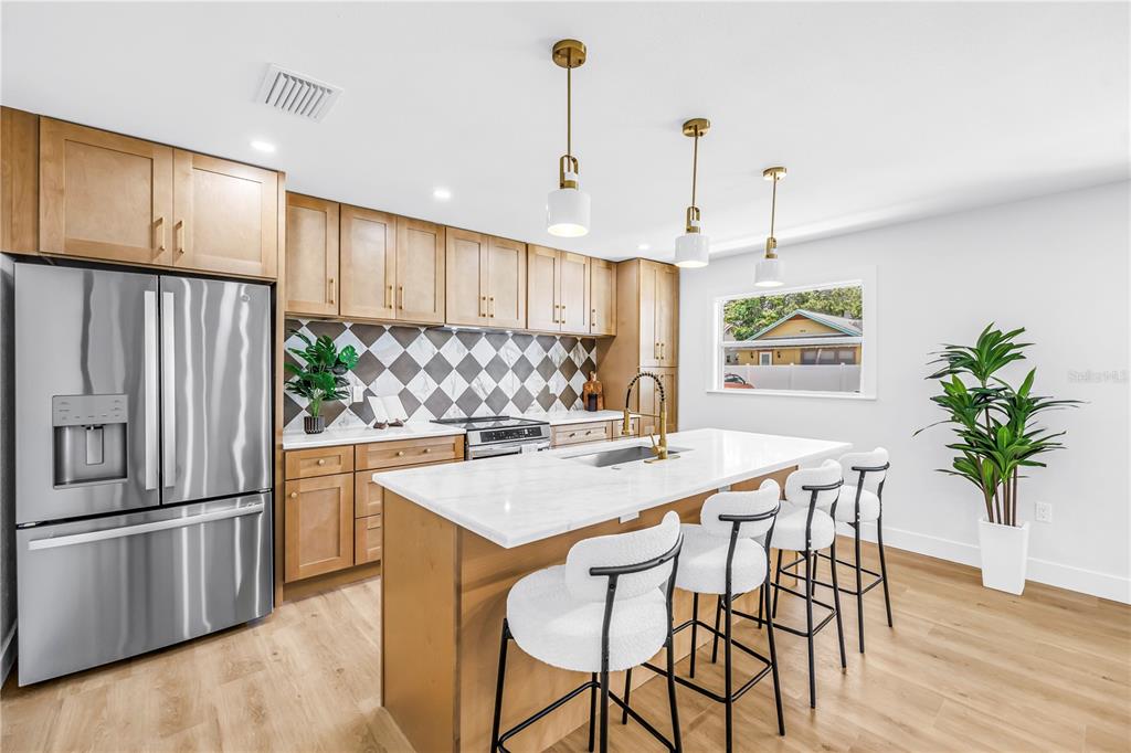 A modern kitchen features light wood cabinets, a marble-topped island with stools, and a backsplash — 1221 36TH TERRACE N, ST PETERSBURG, FL