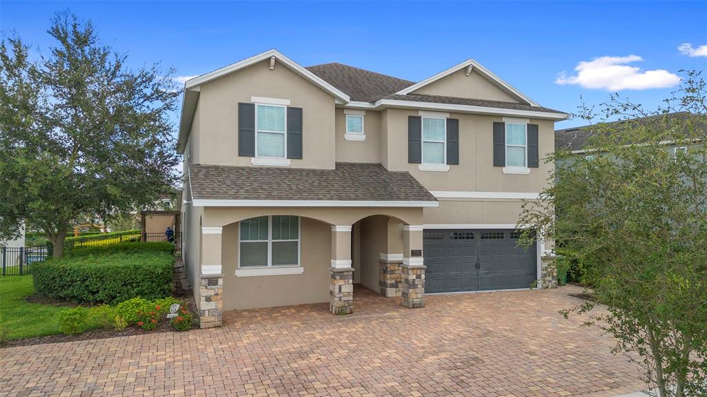 A two-story house with a beige stucco exterior, stone-accented columns, and a paved driveway — 7721 FAIRFAX DRIVE, KISSIMMEE, FL