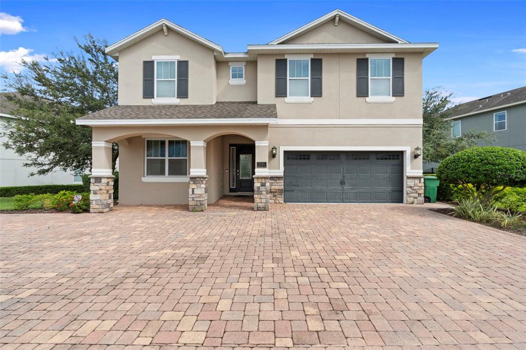 A two-story suburban house with a stone-accented porch, gray garage door, and paver driveway — 7721 FAIRFAX DRIVE, KISSIMMEE, FL