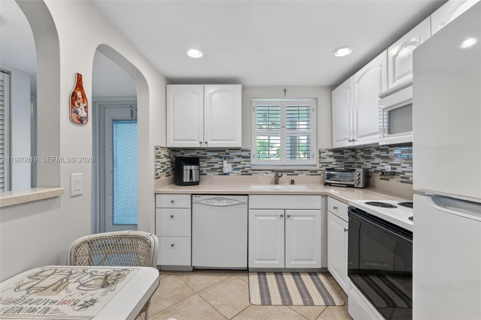 A kitchen features white cabinets, a white appliance suite, and a multi-colored tile backsplash — 6650 Royal Palm Blvd # 207C, Margate FL 33063, MARGATE, FL