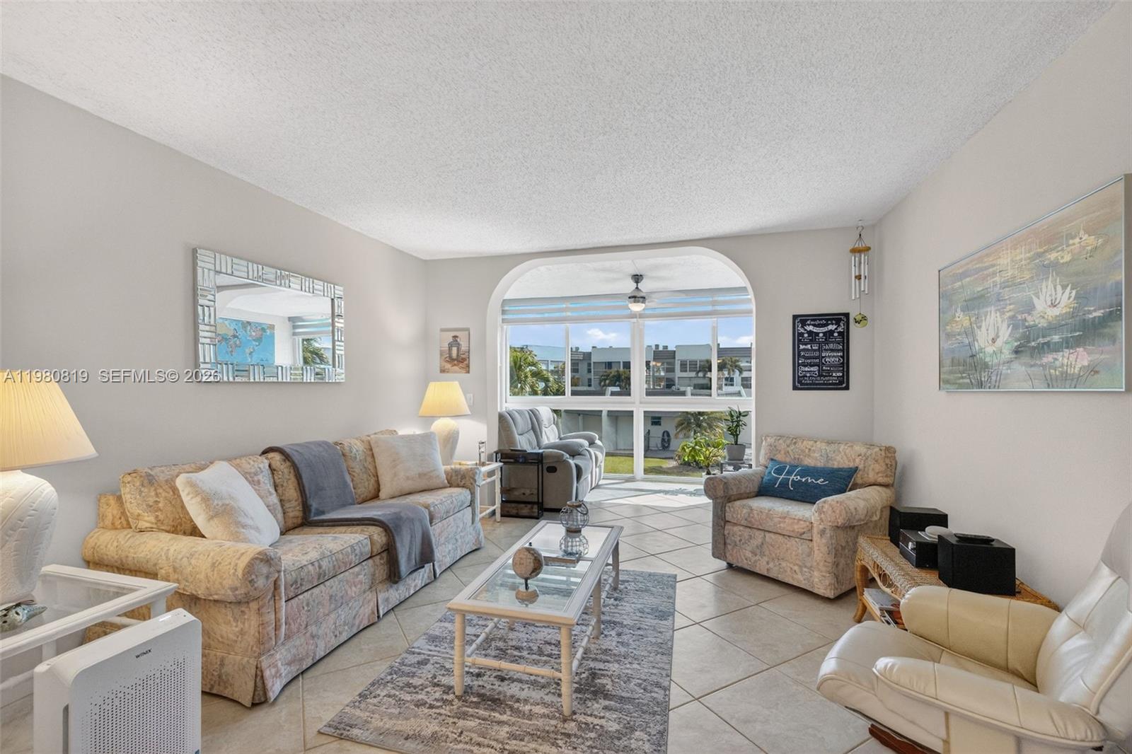 A living room features a floral sofa, tiled floors, and a large arched window view — 6650 Royal Palm Blvd # 207C, Margate FL 33063, MARGATE, FL