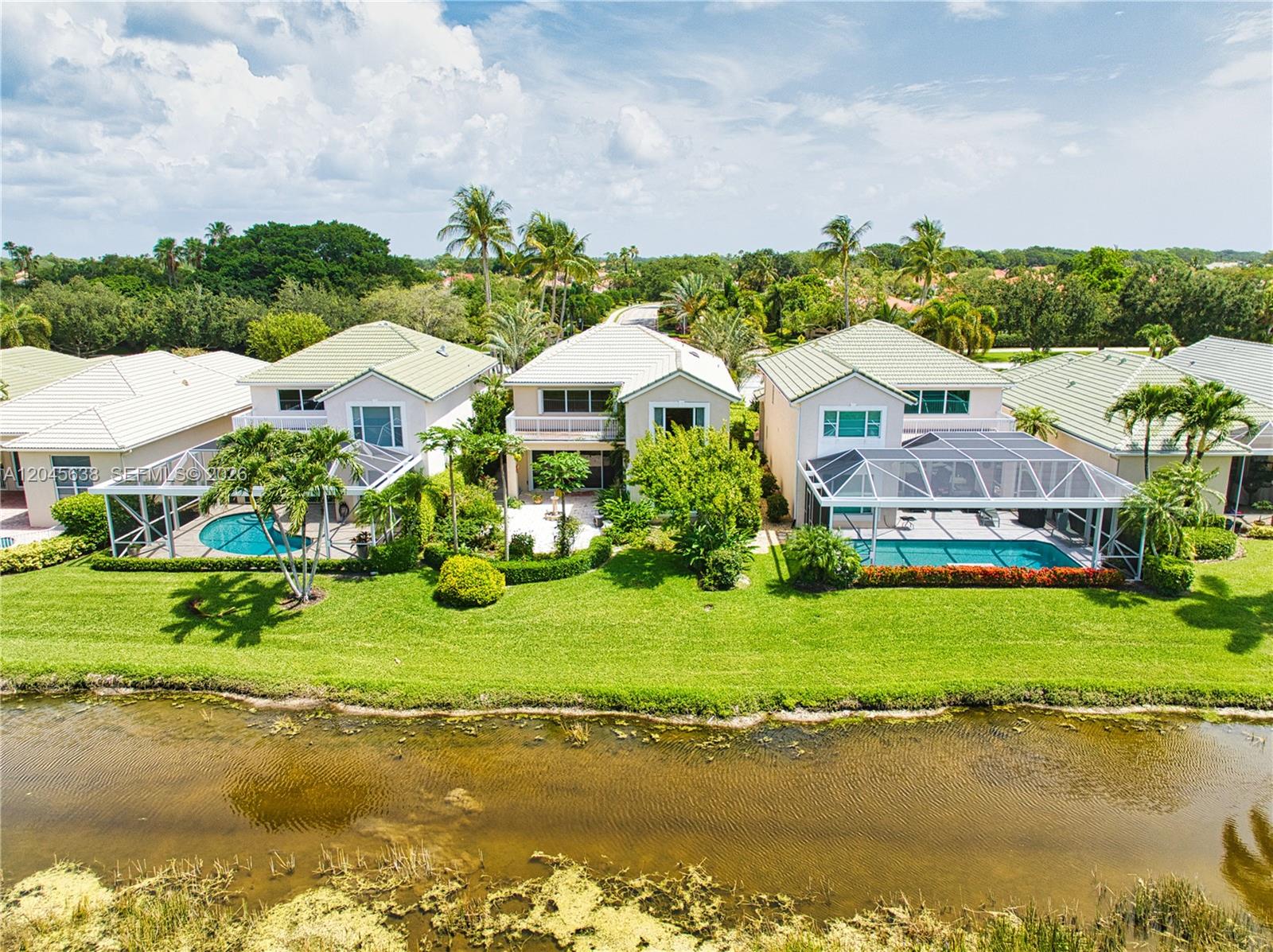An aerial view shows three suburban houses with swimming pools along a grassy canal bank — 1207 General Pointe Trce, Palm Beach Gardens FL 33418, PALM BEACH GARDENS, FL