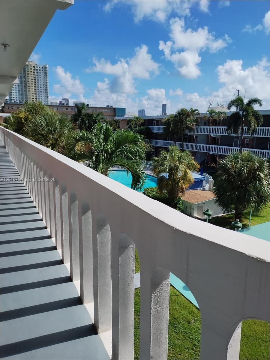 A view from a balcony overlooking a swimming pool, palm trees, and apartment buildings — 201 NE 14th Ave # 10C, Hallandale Beach FL 33009, HALLANDALE BEACH, FL