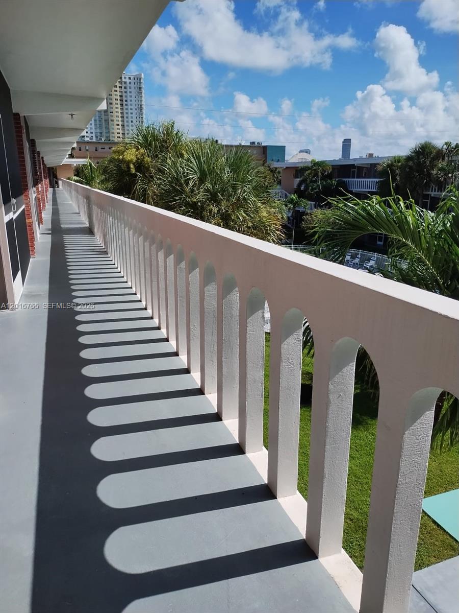 A long outdoor balcony features arched white railings casting shadows on a gray floor — 201 NE 14th Ave # 10C, Hallandale Beach FL 33009, HALLANDALE BEACH, FL
