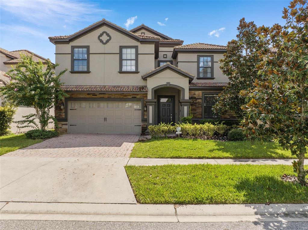 A two-story suburban house with a beige stucco exterior, stone accents, and a two-car garage — 1425 WEXFORD WAY, DAVENPORT, FL