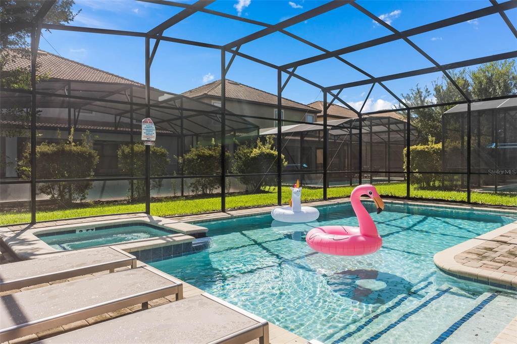 A screened-in swimming pool and hot tub are located in a backyard with lounge chairs — 1425 WEXFORD WAY, DAVENPORT, FL