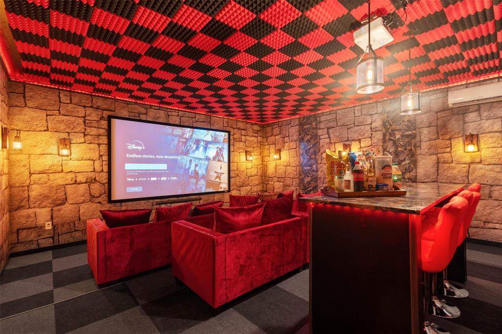 A home theater room features stone walls, a checkered ceiling, red velvet seating, and a bar — 1425 WEXFORD WAY, DAVENPORT, FL