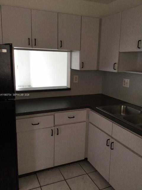 A kitchen features white cabinets, dark countertops, a black refrigerator, and a pass-through window — 1855 W 60th St # 423C, Hialeah FL 33012, HIALEAH, FL