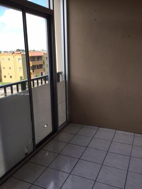 A balcony with white tile flooring and sliding glass doors overlooking a neighboring apartment building — 1855 W 60th St # 423C, Hialeah FL 33012, HIALEAH, FL