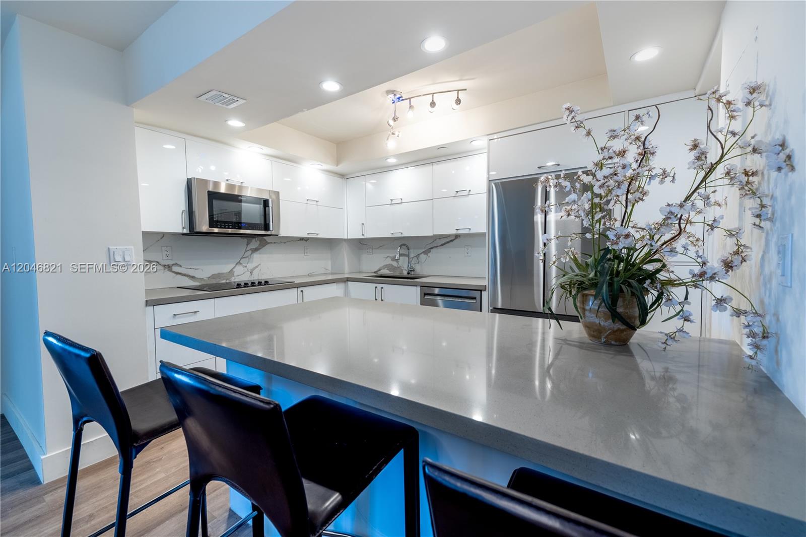 A modern kitchen features white cabinets, gray countertops, stainless steel appliances, and a breakfast bar — 2000 Towerside Ter # 1910, Miami FL 33138, MIAMI, FL
