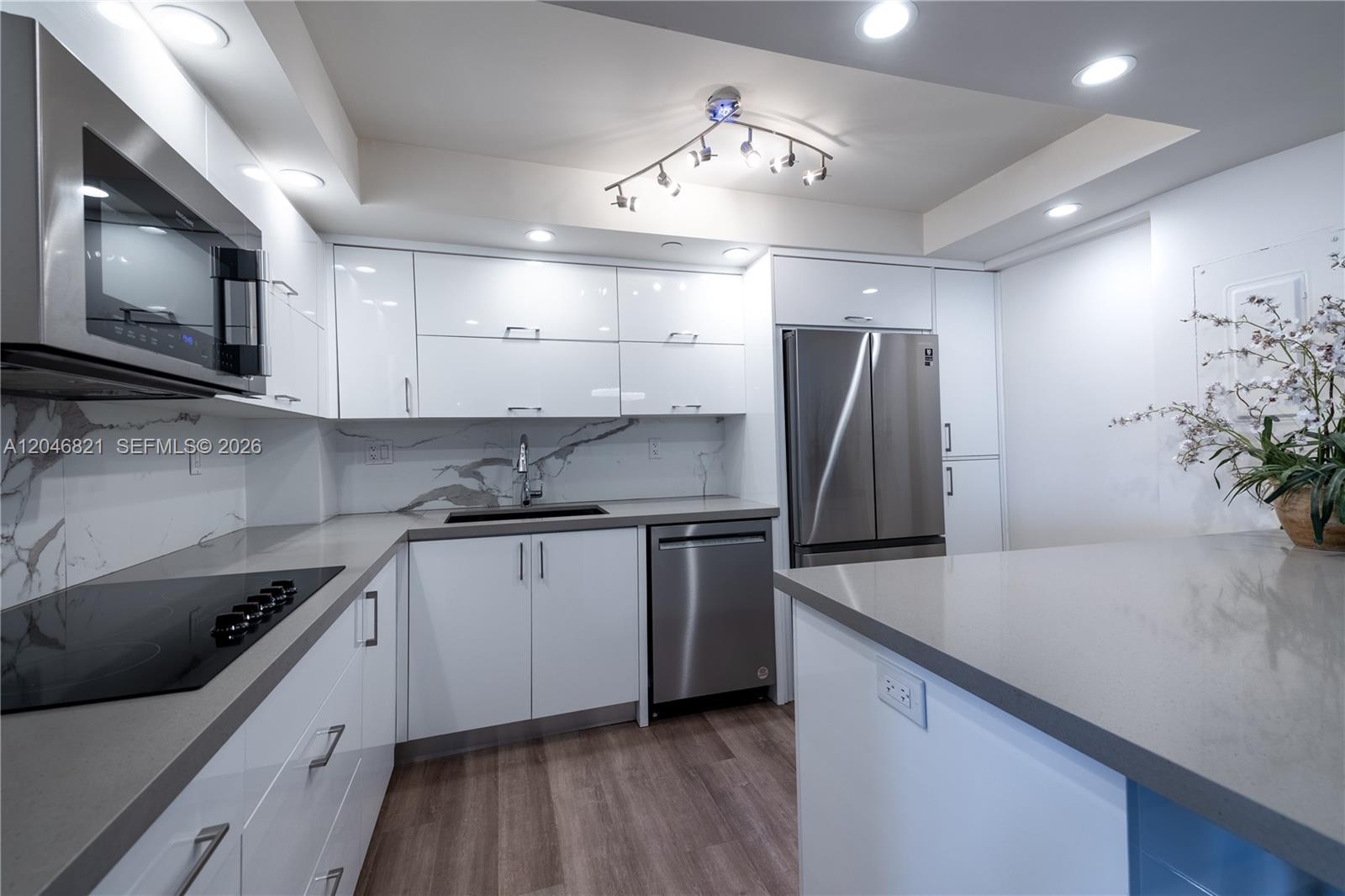 A modern kitchen features white high-gloss cabinets, stainless steel appliances, and gray quartz countertops — 2000 Towerside Ter # 1910, Miami FL 33138, MIAMI, FL