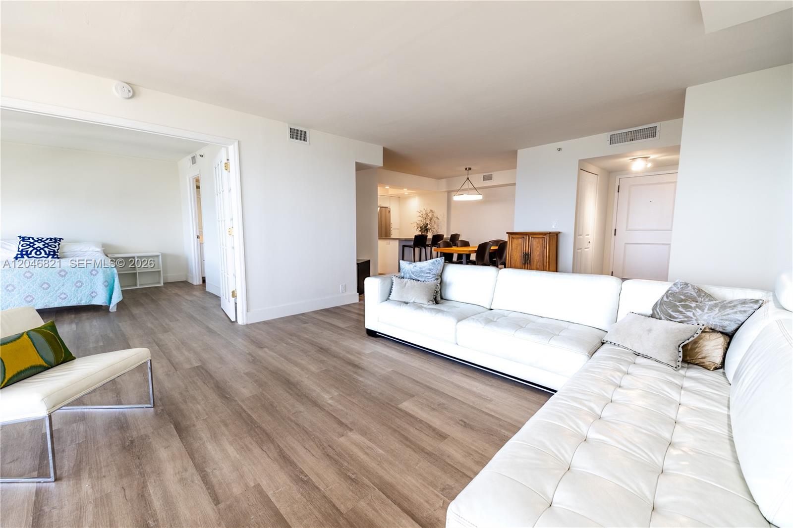 A bright living room features light wood-look flooring, a white sectional sofa, and an open kitchen — 2000 Towerside Ter # 1910, Miami FL 33138, MIAMI, FL