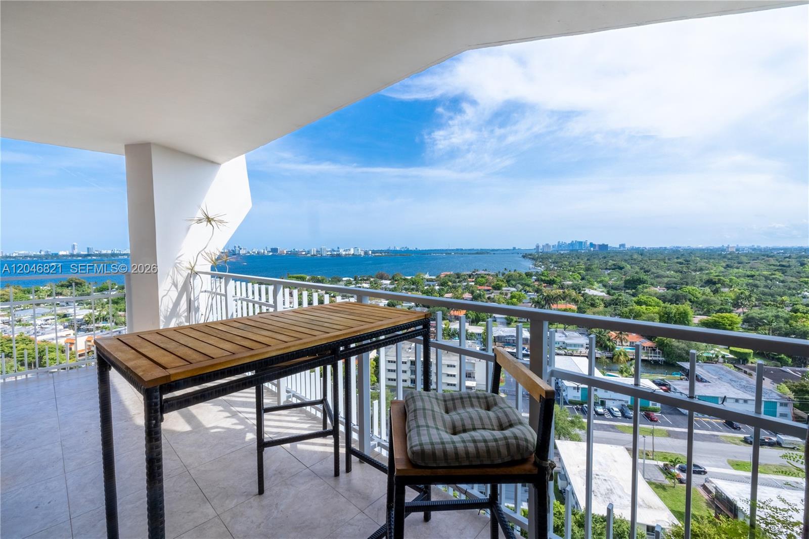 A balcony with a wooden table and chair overlooks a bay and city skyline — 2000 Towerside Ter # 1910, Miami FL 33138, MIAMI, FL