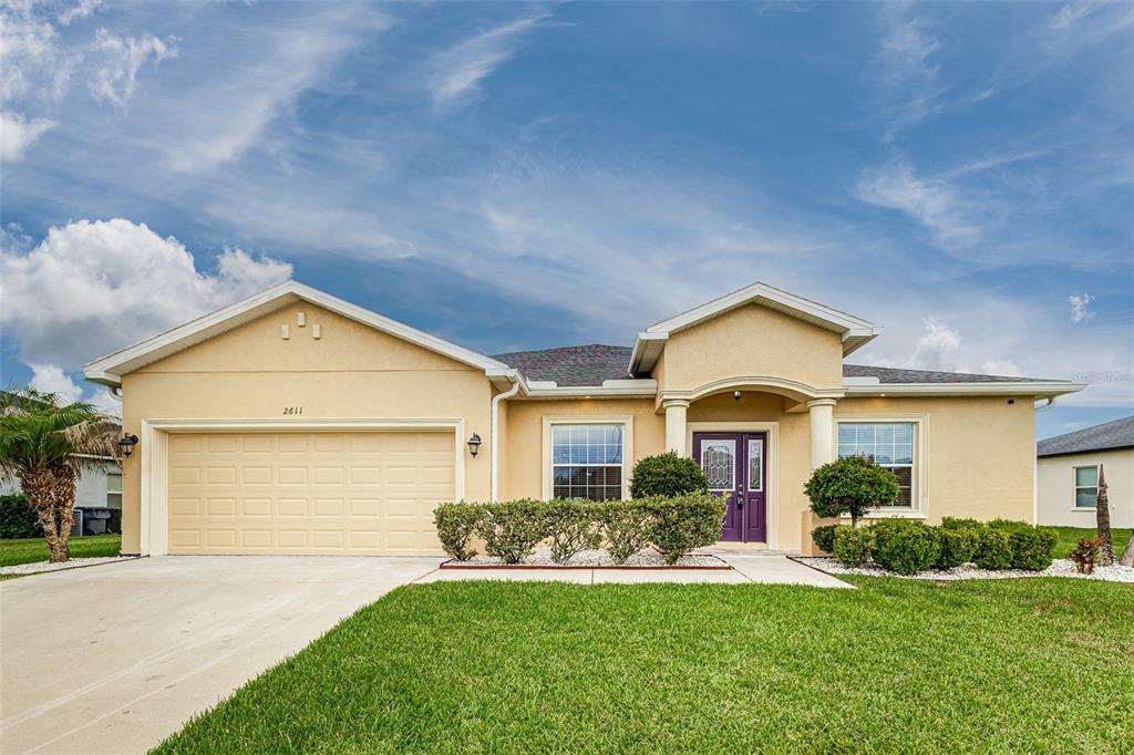 A single-story house with a beige stucco exterior, a two-car garage, and a front lawn — 2611 HIGHLANDS CREEK WAY, LAKELAND, FL