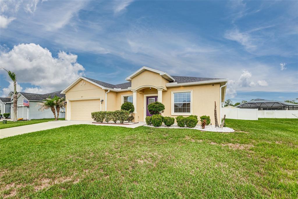 A single-story tan stucco house with a two-car garage and a purple front door — 2611 HIGHLANDS CREEK WAY, LAKELAND, FL