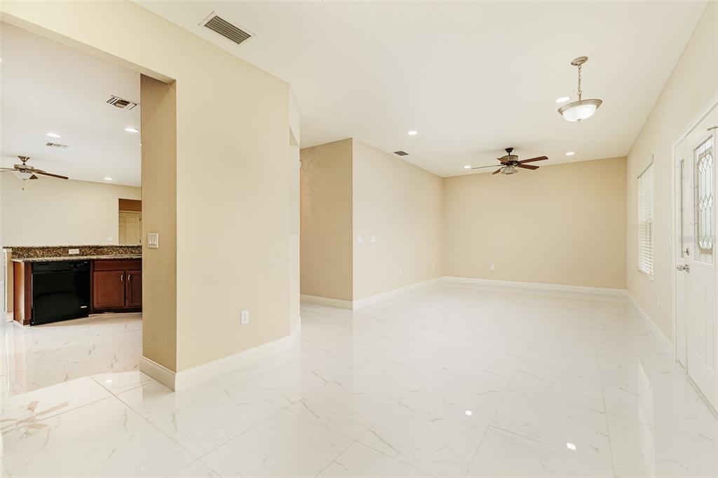 A bright, open-concept living area features white tile flooring, beige walls, and a ceiling fan — 2611 HIGHLANDS CREEK WAY, LAKELAND, FL