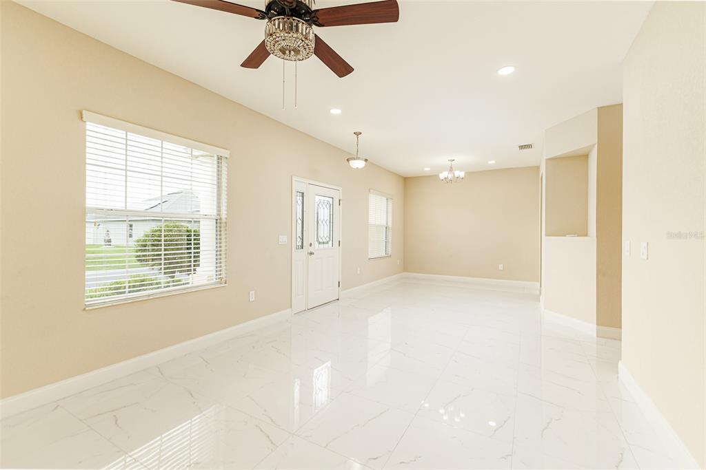 An empty room features white tile flooring, a ceiling fan, and a front entry door — 2611 HIGHLANDS CREEK WAY, LAKELAND, FL