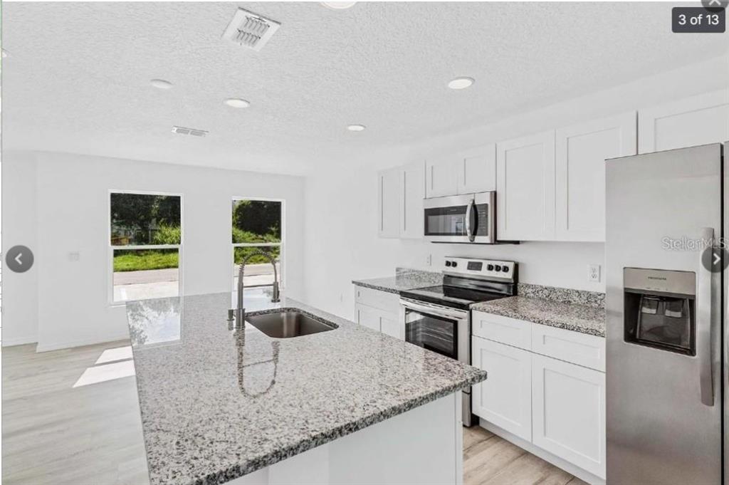 A modern kitchen features white cabinets, granite countertops, a center island, and stainless steel appliances — 172 BOWIE LANE UNIT E, KISSIMMEE, FL