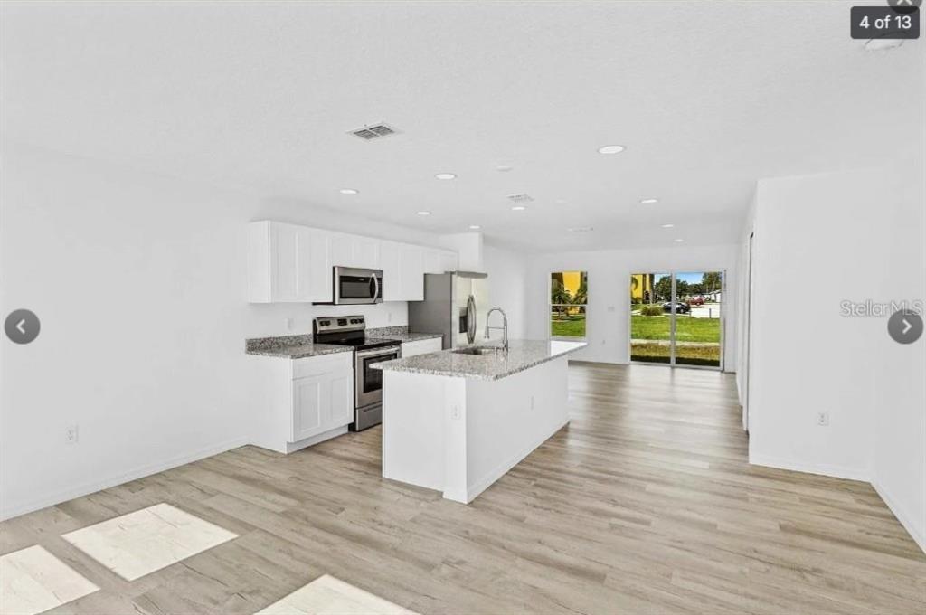 A modern kitchen with white cabinets, granite countertops, and light wood-look flooring — 172 BOWIE LANE UNIT E, KISSIMMEE, FL
