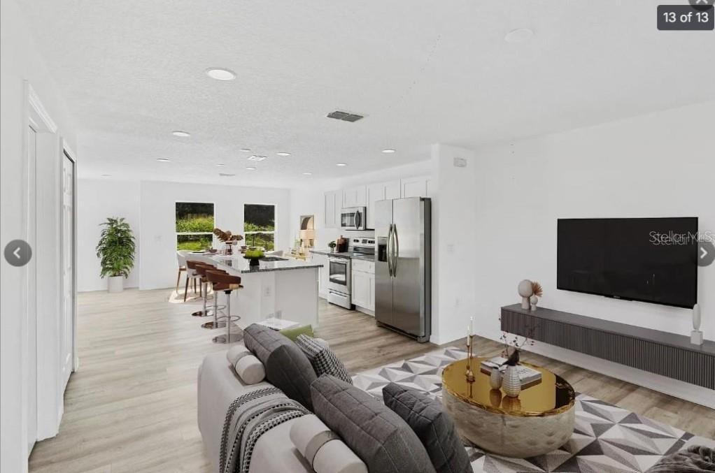 An open-concept living room and kitchen featuring white cabinets, stainless appliances, and light wood flooring — 172 BOWIE LANE UNIT E, KISSIMMEE, FL