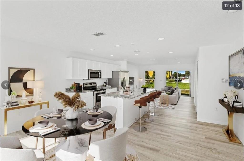 An open-concept kitchen and dining area features white cabinets, granite countertops, and light wood flooring — 172 BOWIE LANE UNIT E, KISSIMMEE, FL