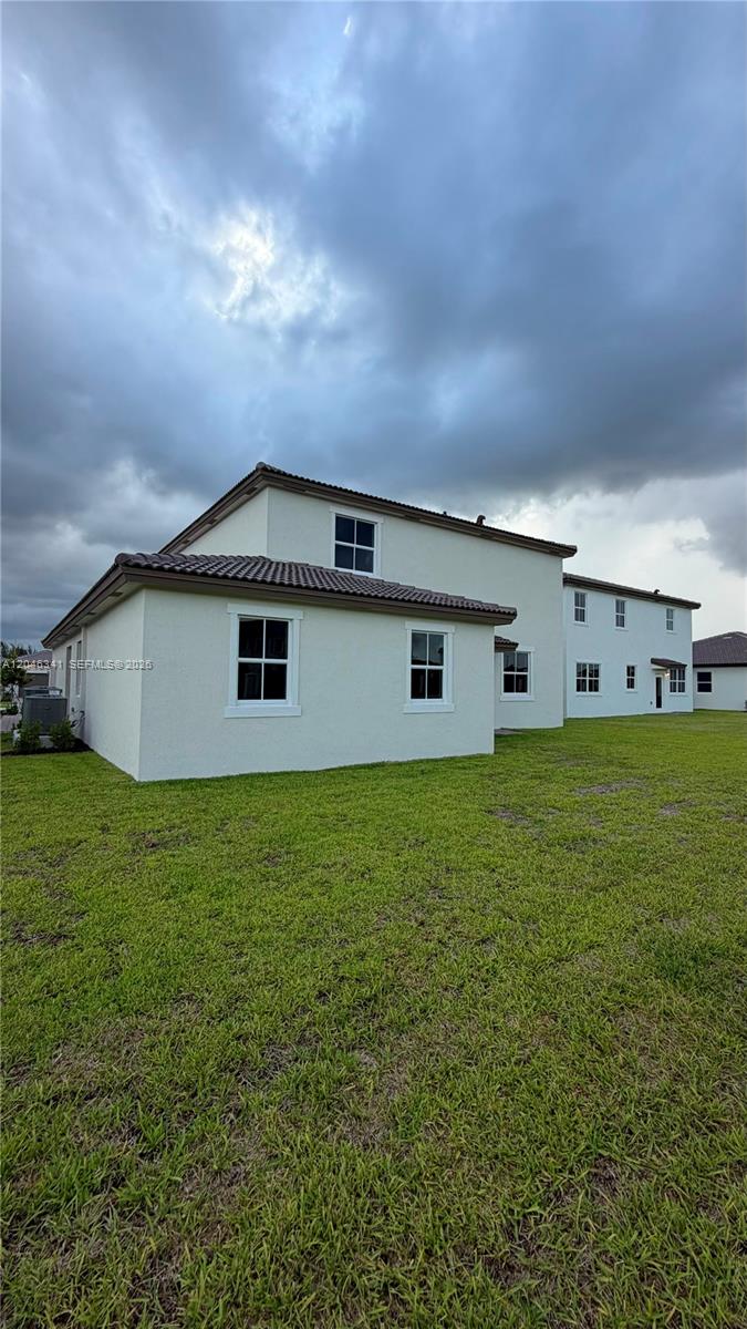 The rear exterior of a two-story beige house features a large lawn under a cloudy sky — 2475 SE 29th Dr, Homestead FL 33035, HOMESTEAD, FL