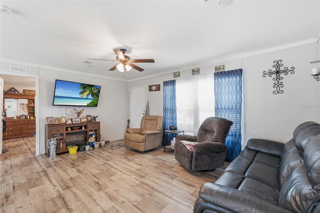 A living room features wood-look flooring, a ceiling fan, a television, and several armchairs — 2086 NW GENES LITTLE ACRES AVENUE, ARCADIA, FL