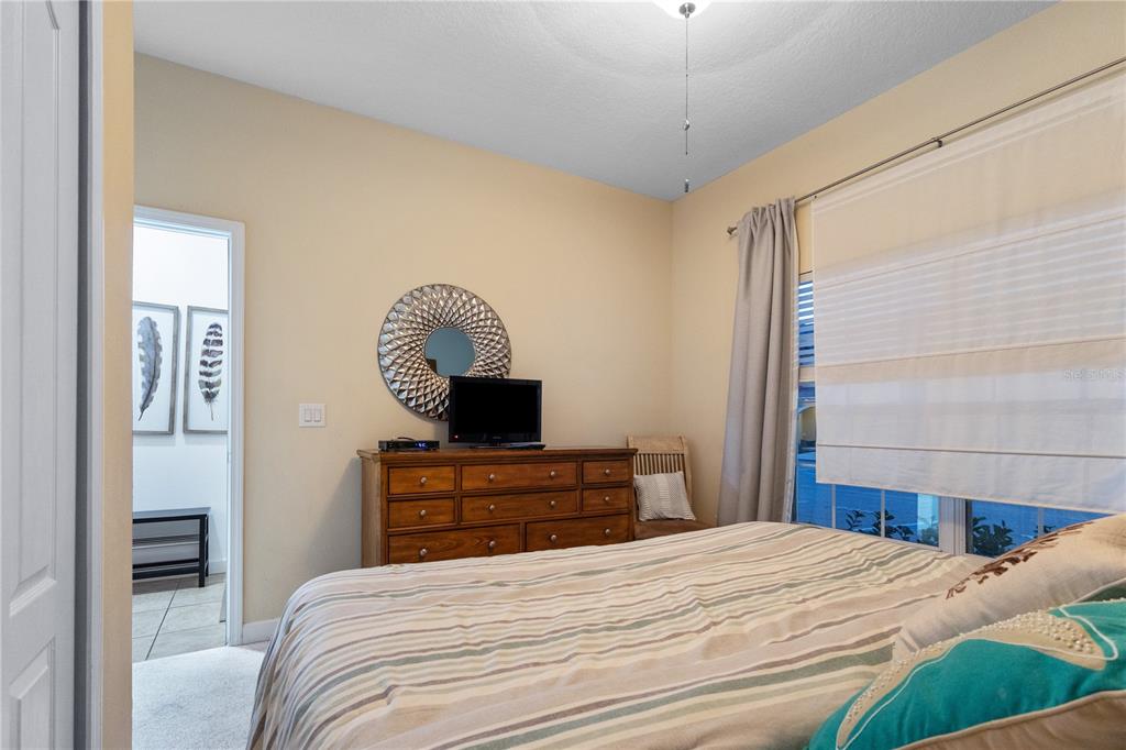 A bedroom features a wooden dresser, a television, a round mirror, and a striped bedspread — 8966 CAT PALM ROAD, KISSIMMEE, FL