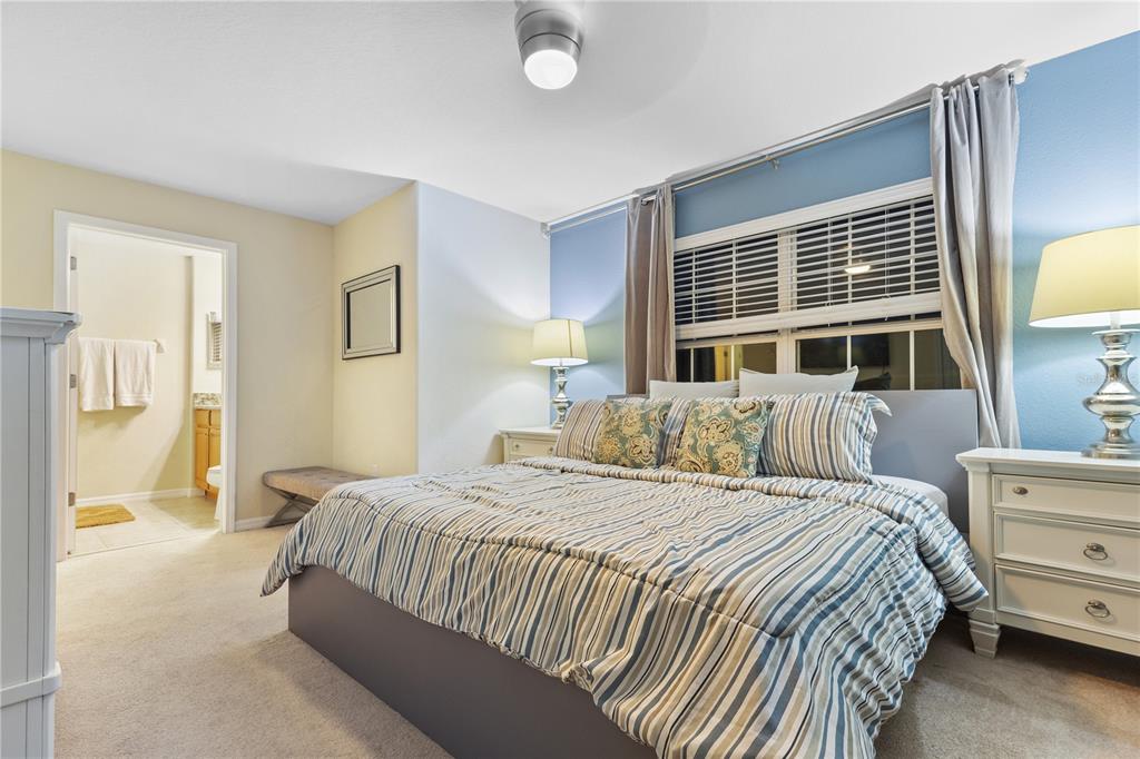 A bedroom features a bed with a striped comforter, two nightstands, and an attached bathroom — 8966 CAT PALM ROAD, KISSIMMEE, FL