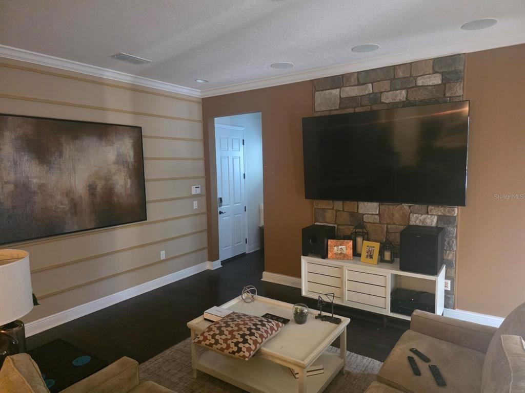 A living room features a stone fireplace wall, horizontal wall molding, and a large television — 9312 HOLLISTON CREEK PLACE, WINTER GARDEN, FL