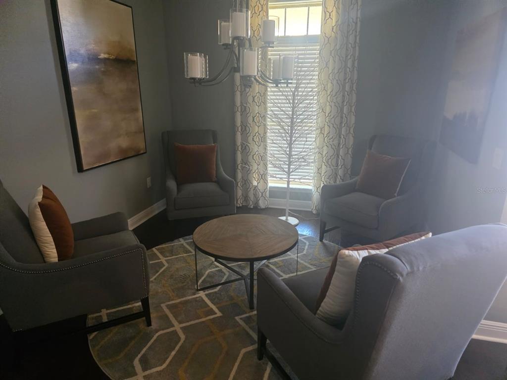 A sitting room features four gray armchairs arranged around a round wooden coffee table — 9312 HOLLISTON CREEK PLACE, WINTER GARDEN, FL