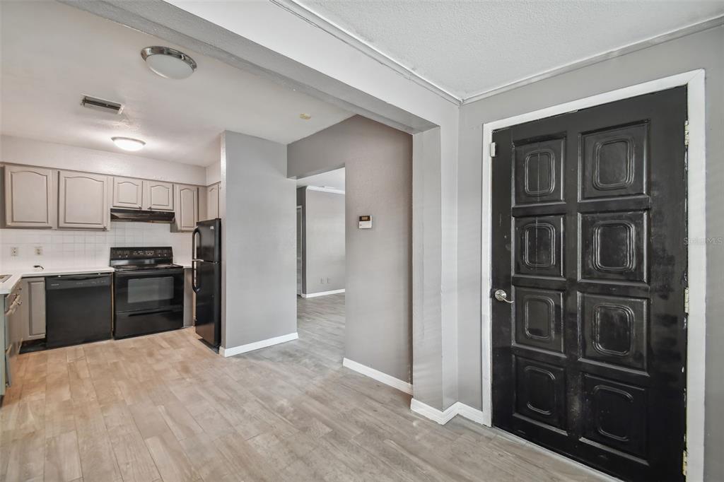 A kitchen with light wood-look flooring, gray cabinets, black appliances, and a black front door — 1921 W STATE STREET, TAMPA, FL