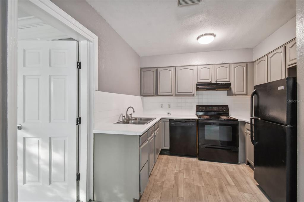 A kitchen features gray cabinets, white countertops, black appliances, and light wood-look flooring — 1921 W STATE STREET, TAMPA, FL