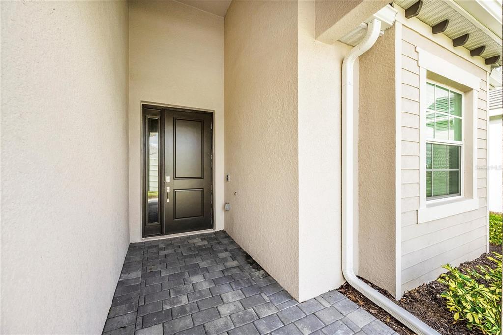 A dark front door with a side window sits under a covered entryway with pavers — 17617 SANTORINI COURT, VENICE, FL