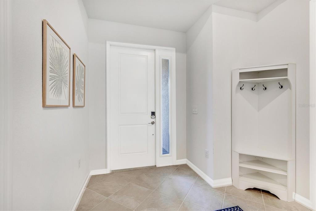 An entryway features a white front door, tiled floor, wall art, and a corner coat rack — 17617 SANTORINI COURT, VENICE, FL